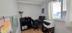 Light-filled room featuring wood-finish flooring, white walls, and a window with white drapes - 