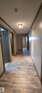 Long hallway featuring wood-finish flooring, neutral wall paint, and contrasting trim - 