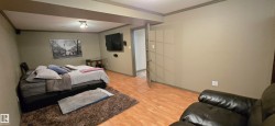 Spacious room featuring wood-finish flooring, neutral-toned walls, and a recessed ceiling with exposed beams - 