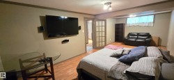 Spacious room featuring wood-finish flooring, a wall-mounted television, and recessed lighting - 