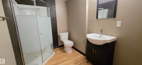 Bathroom with a stand-up shower featuring frosted glass, a white toilet, and wood-finish flooring - 4233 49 Street, Vegreville, AB - Indoor Photo Showing Bathroom