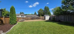 Expansive backyard featuring a lush lawn, perimeter wood fencing, and a storage shed - 