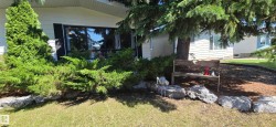 Front yard landscaping featuring mature evergreen trees, manicured shrubs, a rock border, and a grass lawn - 