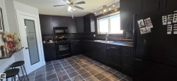 Spacious kitchen featuring dark cabinetry, black tile flooring, a black appliance suite, and a multi-light track lighting fixture - 