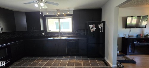 Contemporary kitchen featuring dark cabinetry and countertops, a stainless steel sink with a gooseneck faucet, a black dishwasher, and coordinating tile flooring - 4233 49 Street, Vegreville, AB - Indoor