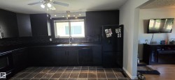 Contemporary kitchen featuring dark cabinetry and countertops, a stainless steel sink with a gooseneck faucet, a black dishwasher, and coordinating tile flooring - 