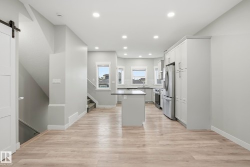 Open-concept kitchen and living area featuring wood-finish flooring, white shaker cabinetry, stainless steel appliances, a center island with countertop seating, and recessed lighting - 36 150 Everitt Dr, St. Albert, AB - Indoor Photo Showing Kitchen