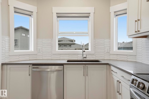 Kitchen featuring white cabinetry, dark countertops, and a full tile backsplash - 36 150 Everitt Dr, St. Albert, AB - Indoor Photo Showing Kitchen