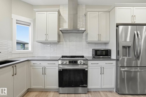 Modern kitchen featuring white shaker-style cabinetry, stainless steel appliances, a grey countertop, and a white picket tile backsplash - 36 150 Everitt Dr, St. Albert, AB - Indoor Photo Showing Kitchen With Stainless Steel Kitchen With Upgraded Kitchen