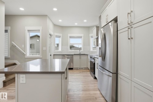 Modern kitchen featuring a central island with a stone-finish countertop, light-toned cabinetry, stainless steel appliances, and wood-finish flooring - 36 150 Everitt Dr, St. Albert, AB - Indoor Photo Showing Kitchen With Upgraded Kitchen