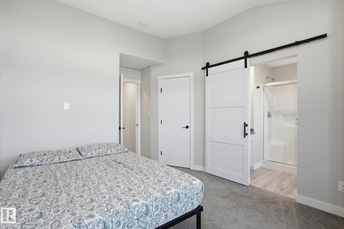 Bedroom featuring light gray walls, gray carpeting, and a white barn door leading to an attached bathroom - 36 150 Everitt Dr, St. Albert, AB - Indoor Photo Showing Bedroom