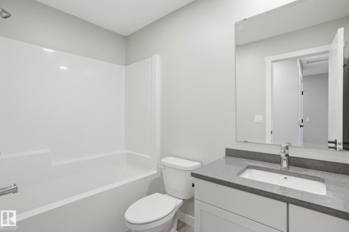 Bathroom featuring a built-in tub/shower combination, a vanity with a dark countertop, a rectangular undermount sink, and a wall-mounted mirror - 36 150 Everitt Dr, St. Albert, AB - Indoor Photo Showing Bathroom