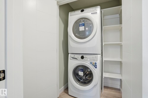 Laundry closet featuring a stacked washer and dryer, built-in shelving, and light wood-finish flooring - 36 150 Everitt Dr, St. Albert, AB - Indoor Photo Showing Laundry Room