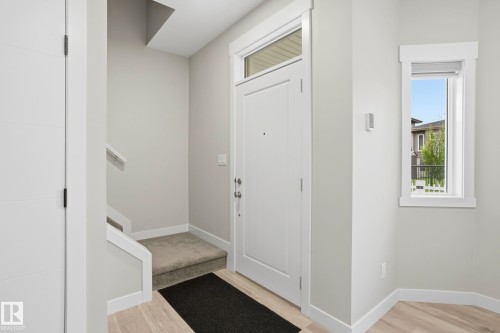 Entryway featuring a white paneled door with transom window, light wood-finish flooring, a small window, and a carpeted stairwell - 36 150 Everitt Dr, St. Albert, AB - Indoor Photo Showing Other Room