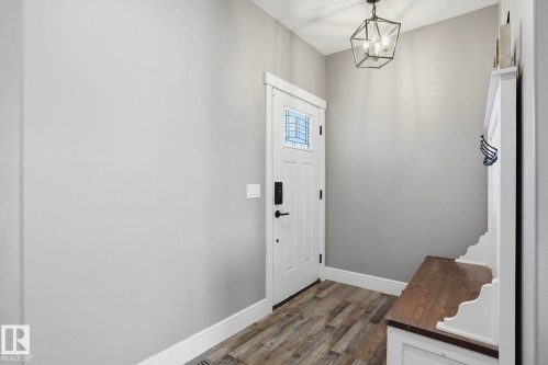 Entryway featuring a white paneled door with decorative glass inlay, an overhead geometric light fixture, wood-finish flooring, and a built-in white bench with a dark wood-finish top - 14 Copperhaven Drive, Spruce Grove, AB 