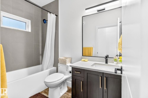 Full bathroom featuring a dark wood-finish vanity with a light-toned countertop, a black-framed mirror, and a tub with a tiled surround - 423 42 Street, Edmonton, AB 