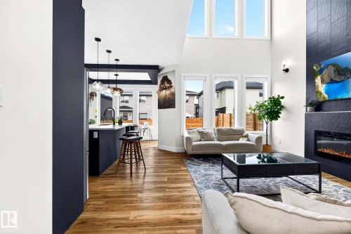 Bright living space featuring wood-finish flooring, a two-story ceiling, and a prominent fireplace with dark stone-look tile surround - 423 42 Street, Edmonton, AB 