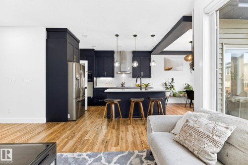 Modern kitchen featuring dark cabinetry, stainless steel appliances, a center island with seating, and pendant lighting - 423 42 Street, Edmonton, AB 