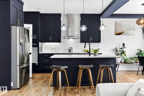 Modern kitchen featuring navy cabinetry, stainless steel appliances, a center island with countertop seating, wood-finish flooring, and pendant lighting - 423 42 Street, Edmonton, AB 