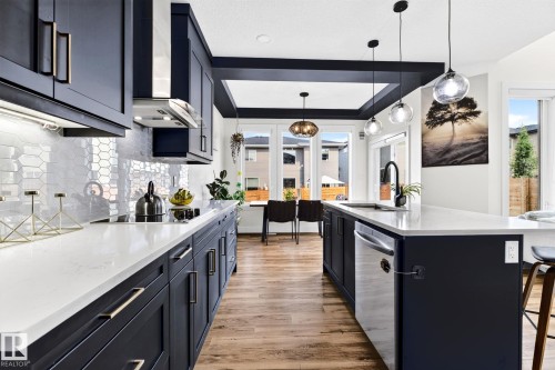 Contemporary kitchen featuring dark cabinetry with gold-tone hardware, white countertops, a patterned backsplash, and wood-finish flooring - 423 42 Street, Edmonton, AB 