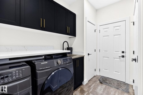 Laundry area featuring black cabinetry with gold-tone hardware, a white countertop, and an integrated utility sink with a matte black faucet - 423 42 Street, Edmonton, AB 