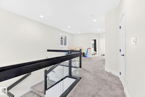 Open hallway featuring a contemporary glass and black metal railing system, recessed lighting, and soft grey carpet flooring - 423 42 Street, Edmonton, AB 
