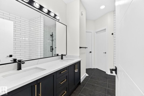 Double vanity with quartz countertops, integrated sinks, matte black faucets, and dark cabinetry with brass hardware - 423 42 Street, Edmonton, AB 
