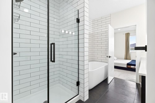Bathroom featuring a frameless glass shower enclosure with matte black hardware, white subway tile walls, a freestanding soaking tub, and dark tile flooring - 423 42 Street, Edmonton, AB 