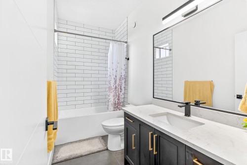 Modern bathroom featuring a dark wood-finish vanity with gold-tone hardware, a white countertop with an integrated rectangular sink, a black-framed mirror, and a linear light fixture - 423 42 Street, Edmonton, AB 