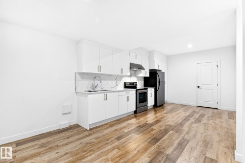 Contemporary kitchen featuring white cabinetry, a white marble-patterned backsplash, stainless steel appliances including a range and over-the-range microwave, and wood-finish flooring - 423 42 Street, Edmonton, AB 