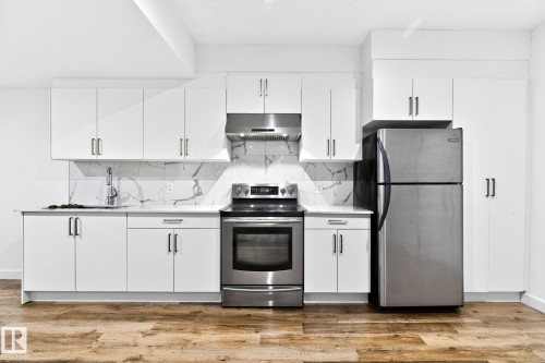 Contemporary kitchen featuring white cabinetry, stainless steel appliances, a white marble-patterned backsplash, light-toned countertops, and wood-finish flooring - 423 42 Street, Edmonton, AB 