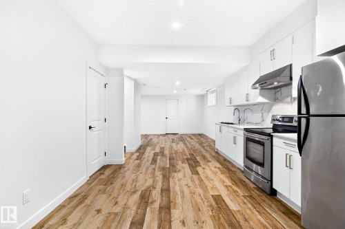 Contemporary kitchen featuring white cabinetry, stainless steel appliances, a marble-look backsplash, and wood-finish flooring - 423 42 Street, Edmonton, AB 