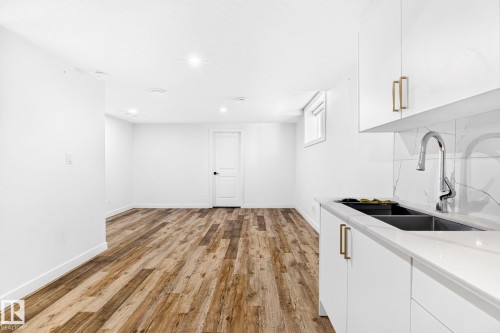 Bright white cabinetry with gold-tone hardware, a double basin sink with a high-arc faucet, and a white countertop with a matching backsplash - 423 42 Street, Edmonton, AB 