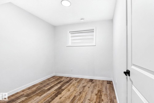 Room featuring wood-finish flooring, white baseboards, a single window with blinds, and a white interior door with black hardware - 423 42 Street, Edmonton, AB 