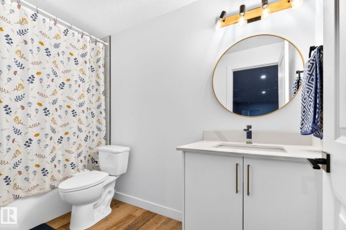 Bathroom featuring a white vanity with a light-toned countertop, a wall-mounted round mirror with a gold-finish frame, and wood-finish flooring - 423 42 Street, Edmonton, AB 
