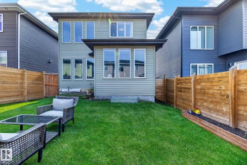 Manicured green lawn with a wooden privacy fence, a raised garden bed, and a two-story residence featuring multiple windows and a lower-level extension - 423 42 Street, Edmonton, AB 