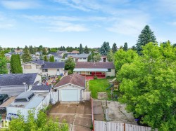 Rear property view featuring a detached garage with a white overhead door, a paved driveway, and a fenced yard with mature trees - 