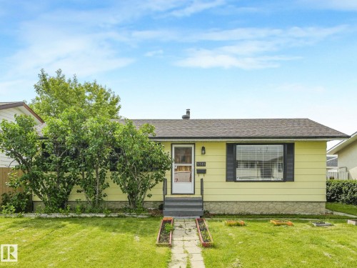 Single-story residence featuring light yellow siding, a dark shingle roof, and a prominent front bay window with dark shutters - 9315 151 Avenue, Edmonton, AB 