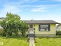 Single-story residence featuring light yellow siding, a dark shingle roof, and a prominent front bay window with dark shutters - 9315 151 Avenue, Edmonton, AB 