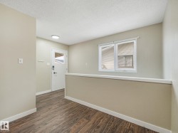 Entryway featuring wood-finish flooring, neutral wall tones, a modern white entry door with glass pane, a built-in wall partition, and a double-pane window with blinds - 
