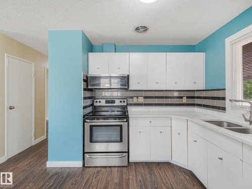 Kitchen featuring white cabinetry, light countertops, wood-finish flooring, stainless steel range, and an integrated microwave - 9315 151 Avenue, Edmonton, AB 