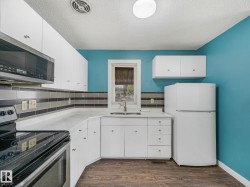 Kitchen featuring wood-finish flooring, white cabinetry, a stainless steel over-the-range microwave, a white refrigerator, and a tiled backsplash - 