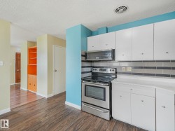 Kitchen featuring stainless steel range and microwave, white cabinetry, light-toned countertops, and a gray-tiled backsplash - 