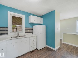 Kitchen area featuring white cabinetry, a double basin sink with a single-handle faucet, a white refrigerator, and wood-finish flooring - 