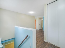 Upper level hallway featuring wood-finish flooring, light blue wall accent, a built-in closet with sliding doors, and a flush mount ceiling light - 