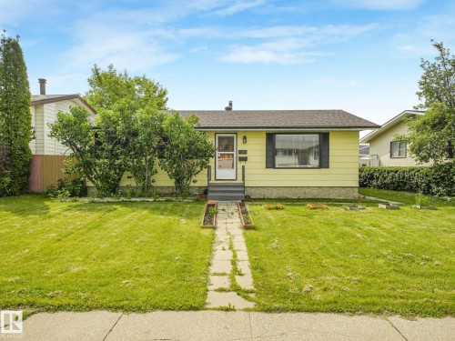 Single-story residence featuring light yellow siding, a dark shingle roof, and a stone foundation - 9315 151 Avenue, Edmonton, AB 