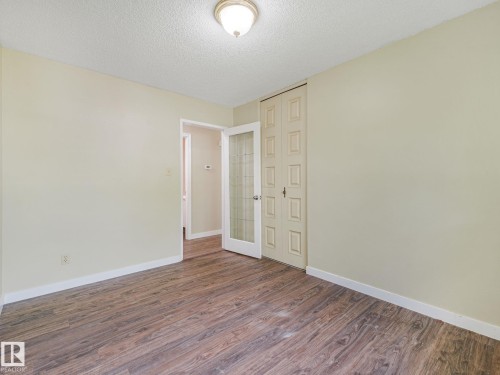 Spacious room featuring wood-finish flooring, light-toned walls, and a textured ceiling - 9315 151 Avenue, Edmonton, AB 