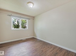 Spacious room featuring wood-finish flooring, light-toned walls, and a large window with white trim - 