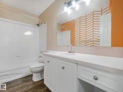 Bathroom featuring a white integrated tub and shower unit, wood-finish flooring, and a vanity with a white countertop, integrated sink, and white cabinetry - 