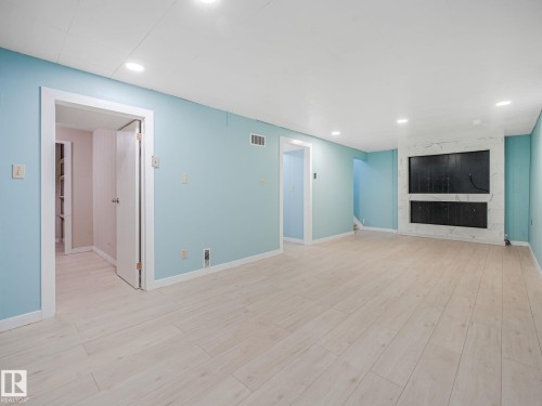 Spacious interior featuring light wood-finish flooring, recessed lighting, and a modern fireplace with a marble-look surround - 9315 151 Avenue, Edmonton, AB 